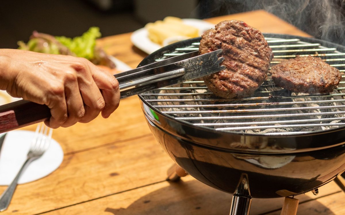 A hand uses tongs to grill burgers on a charcoal barbecue. Perfect for outdoor dining scenes.